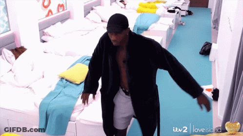 A Man In A Bathrobe Is Dancing In A Room With Lots Of Beds And A Sign That Says Love Island GIF
