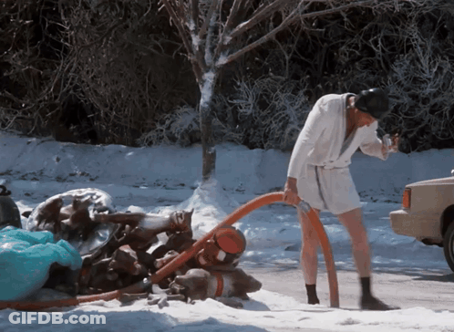 A Man In A Bathrobe Is Pumping Water Out Of A Hose In The Snow GIF
