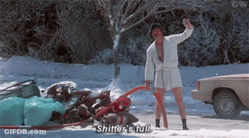 A Man In A Bathrobe Is Standing In The Snow Holding A Vacuum Cleaner And A Bottle . GIF
