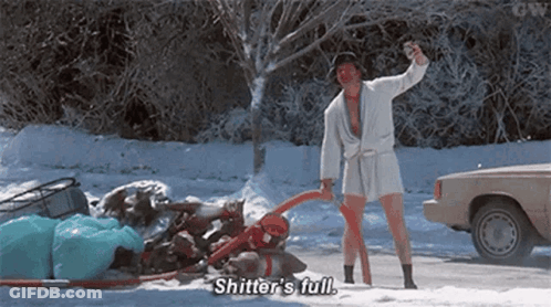 A Man In A Bathrobe Is Standing In The Snow Next To A Car And Holding A Bottle Of Beer . GIF