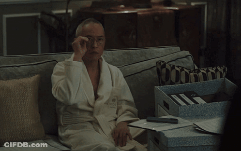 A Man In A Bathrobe Sits On A Couch With A Pillow GIF