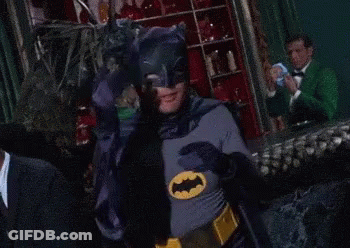 A Man In A Batman Costume Covers His Eyes With His Hands GIF