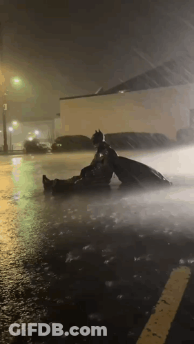 A Man In A Batman Costume Is Laying In The Rain GIF