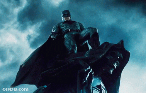 A Man In A Batman Costume Is Sitting On A Statue GIF