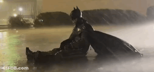 A Man In A Batman Costume Is Sitting On Top Of Another Man In A Puddle Of Water . GIF