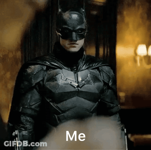 A Man In A Batman Costume Is Standing In A Dark Room And Says Me GIF