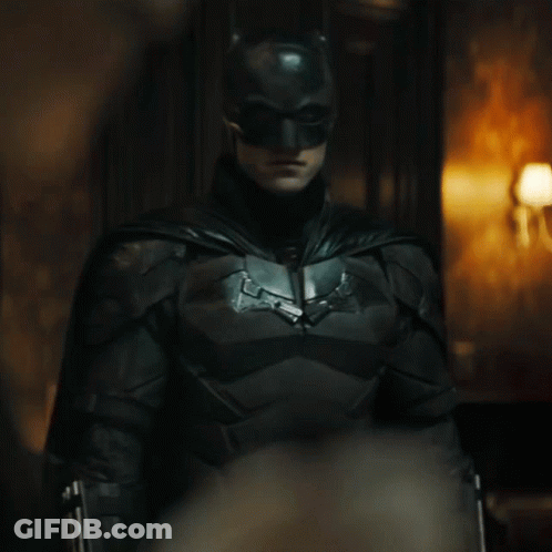A Man In A Batman Costume Is Standing In A Dark Room GIF