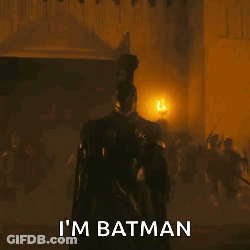 A Man In A Batman Costume Is Standing In Front Of A Group Of People . GIF