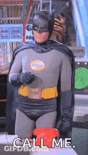 A Man In A Batman Costume Is Standing In Front Of A Red Telephone And Saying `` Call Me '' . GIF