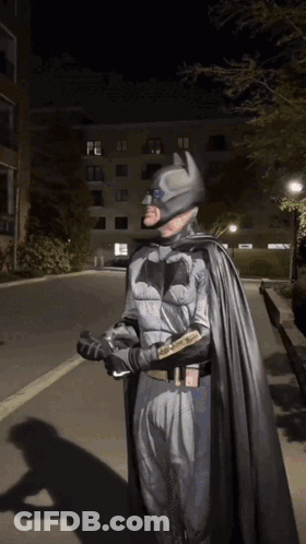 A Man In A Batman Costume Is Walking Down The Street GIF