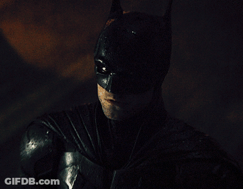 A Man In A Batman Costume Looks At The Camera GIF