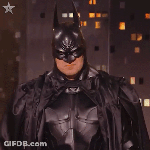 A Man In A Batman Costume Stands In Front Of A Building GIF