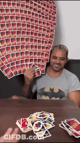 A Man In A Batman Shirt Is Playing Uno GIF