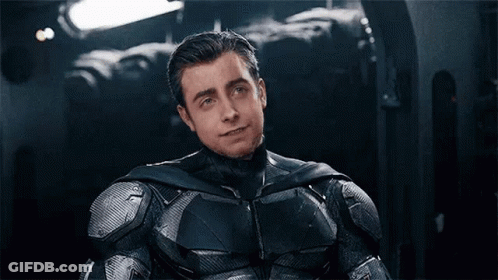 A Man In A Batman Suit Is Sitting Down With His Eyes Closed And Smiling . GIF