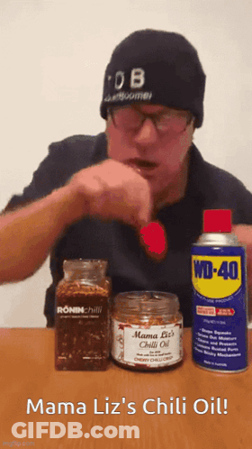 A Man In A Beanie Is Eating A Red Pepper Next To A Can Of Wd-40 GIF