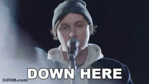 A Man In A Beanie Is Singing Into A Microphone And The Words Down Here Are Above Him . GIF