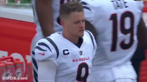 A Man In A Bengals Jersey Is Kneeling Down On The Field . GIF