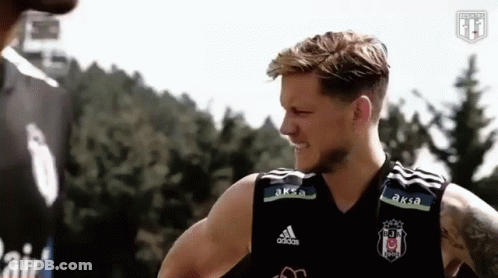 A Man In A Black Adidas Tank Top Is Talking To Another Man In Front Of A Forest . GIF