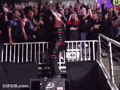 A Man In A Black And Red Outfit Is Jumping Over A Fence In Front Of A Crowd With A Yellow Sign That Says Ps GIF