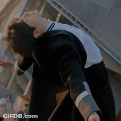A Man In A Black And White Jacket Is Bending Over In Front Of A Building . GIF