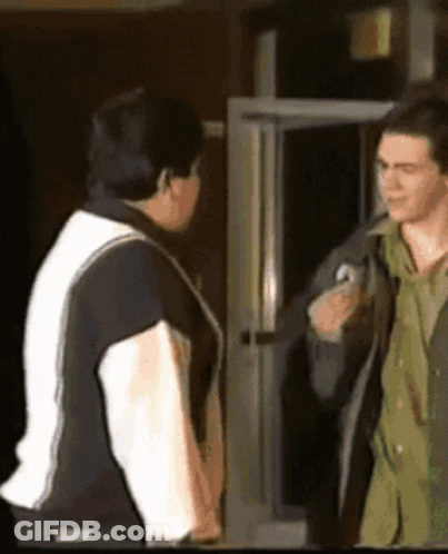 A Man In A Black And White Jacket Is Talking To Another Man GIF