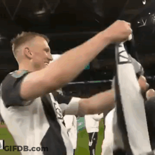 A Man In A Black And White Shirt Holds Up A Scarf With The Letter A On It GIF