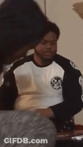 A Man In A Black And White Shirt Is Sitting At A Table With A Woman Behind Him . GIF