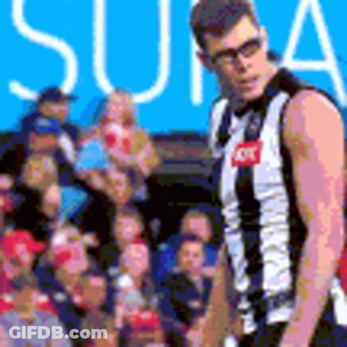 A Man In A Black And White Striped Jersey Is Standing In Front Of A Crowd Of People . GIF