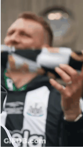 A Man In A Black And White Striped Shirt Is Drinking A Bottle Of Water . GIF