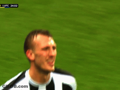 A Man In A Black And White Striped Shirt Is Making A Funny Face On A Soccer Field GIF