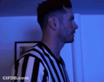 A Man In A Black And White Striped Shirt Stands In A Dark Room GIF