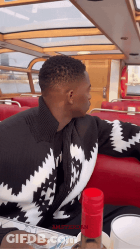 A Man In A Black And White Sweater Sits On A Boat With The Word Amsterdam On The Bottom GIF