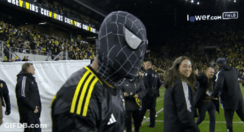 A Man In A Black And Yellow Spider Man Costume Stands On A Field GIF