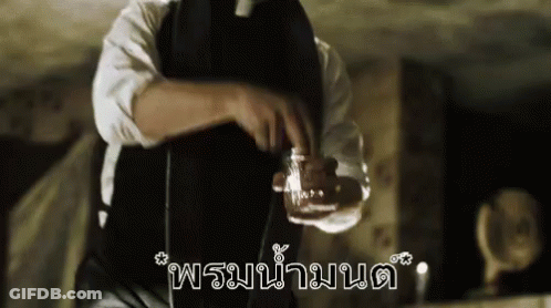 A Man In A Black Apron Is Holding A Glass Of Liquid In His Hand . GIF