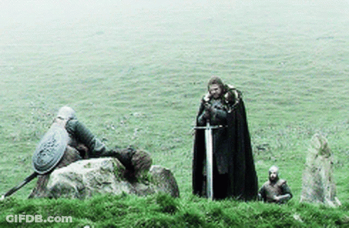 A Man In A Black Cape Holding A Sword Stands In A Grassy Field GIF