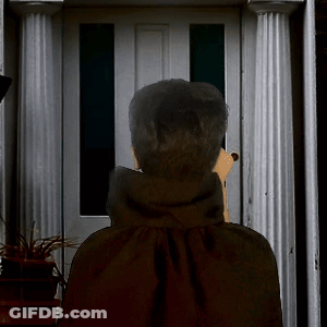 A Man In A Black Cape Stands In Front Of A Door Talking On A Cell Phone GIF