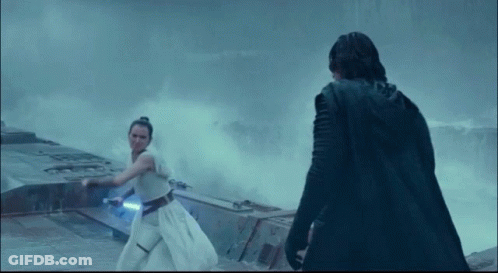 A Man In A Black Cape Stands Next To A Woman Holding A Light Saber GIF