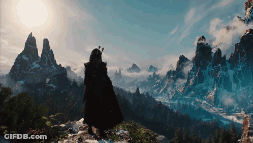 A Man In A Black Cape Stands On Top Of A Mountain GIF