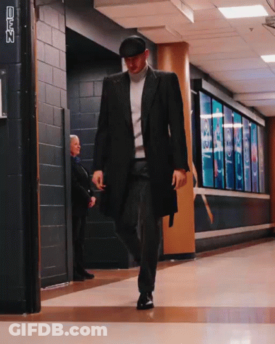 A Man In A Black Coat And Hat Walks Down A Hallway With A Sign That Says Cnn On It GIF