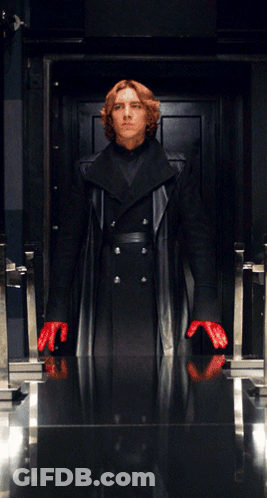 A Man In A Black Coat And Red Gloves Stands In A Doorway GIF