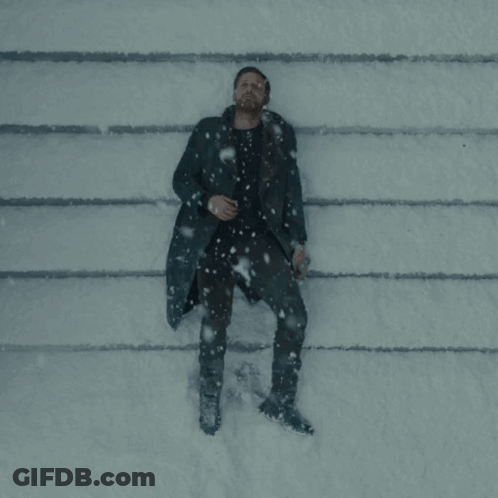 A Man In A Black Coat Is Laying On The Ground In The Snow GIF