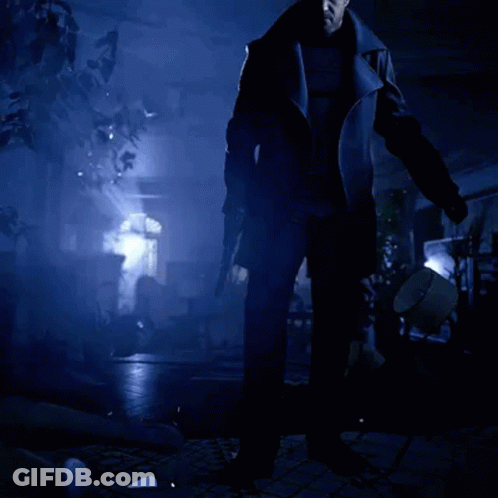 A Man In A Black Coat Is Standing In A Dark Room Holding A Gun GIF