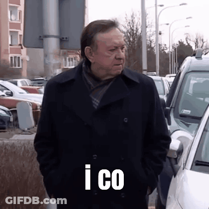 A Man In A Black Coat Is Standing In A Parking Lot With His Hands In His Pockets And The Words I Co On His Chest GIF