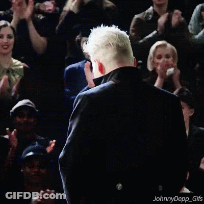 A Man In A Black Coat Is Standing In Front Of A Crowd Of People . GIF