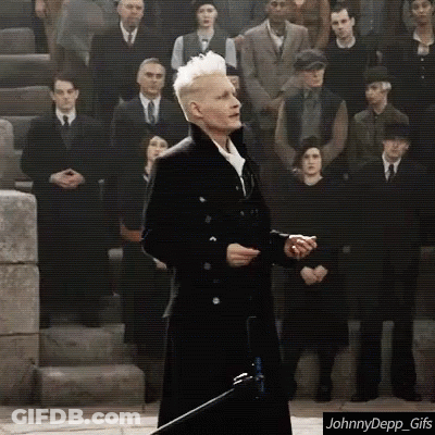 A Man In A Black Coat Is Standing In Front Of A Crowd Of People . GIF