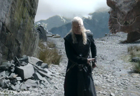 A Man In A Black Coat Is Standing In Front Of A Large Dragon GIF