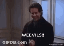 A Man In A Black Coat Is Standing In Front Of A Window Holding A Knife And Saying Weevils ! GIF