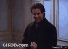 A Man In A Black Coat Is Standing In Front Of A Window Holding Something In His Hand . GIF