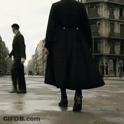 A Man In A Black Coat Is Walking Down A Wet Street GIF
