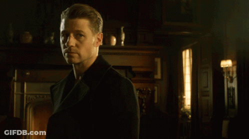 A Man In A Black Coat Stands In Front Of A Fireplace In A Dark Room GIF
